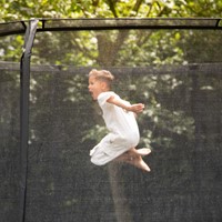 Lifestyle afbeelding van een kind dat springt op de VirtuFit Premium Trampoline met een stevig veiligheidsnet in een groene tuin.